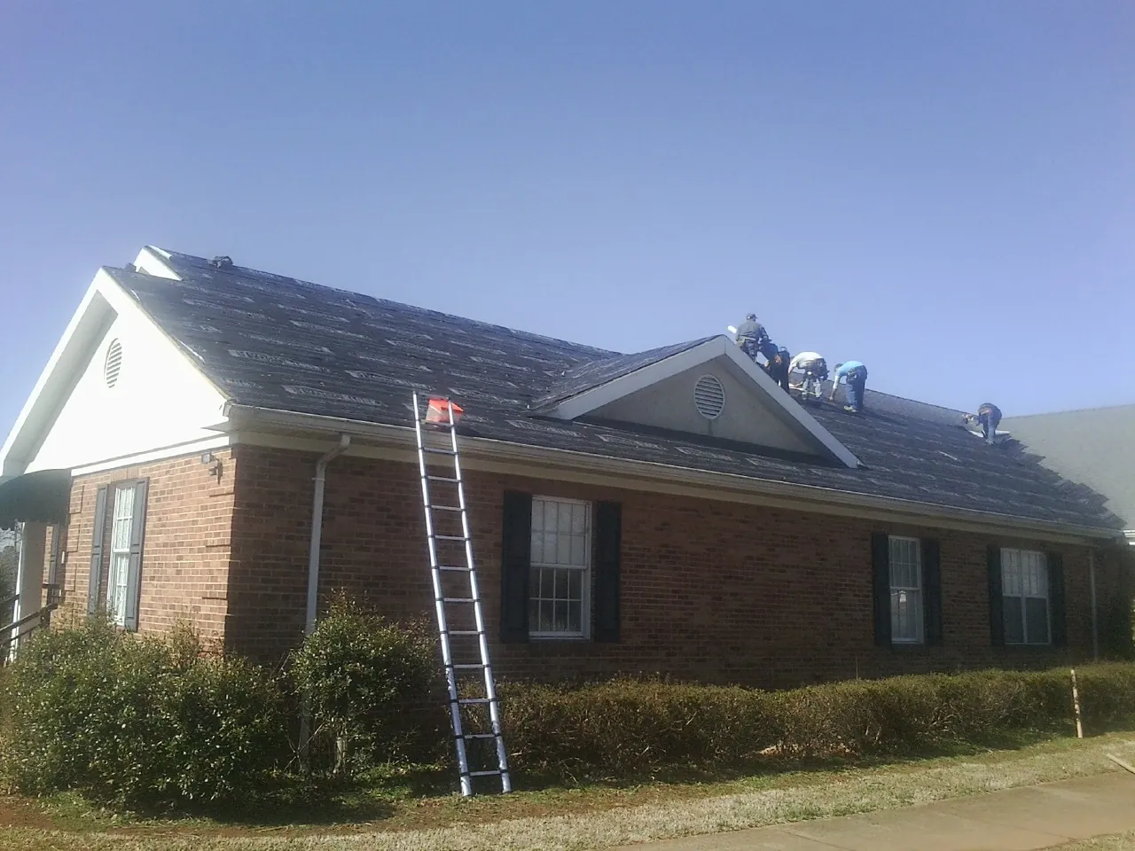 Crew tearing shingles off a brick ranch roof with a ladder set — Emergency Roof Repair work by our crew in Bee